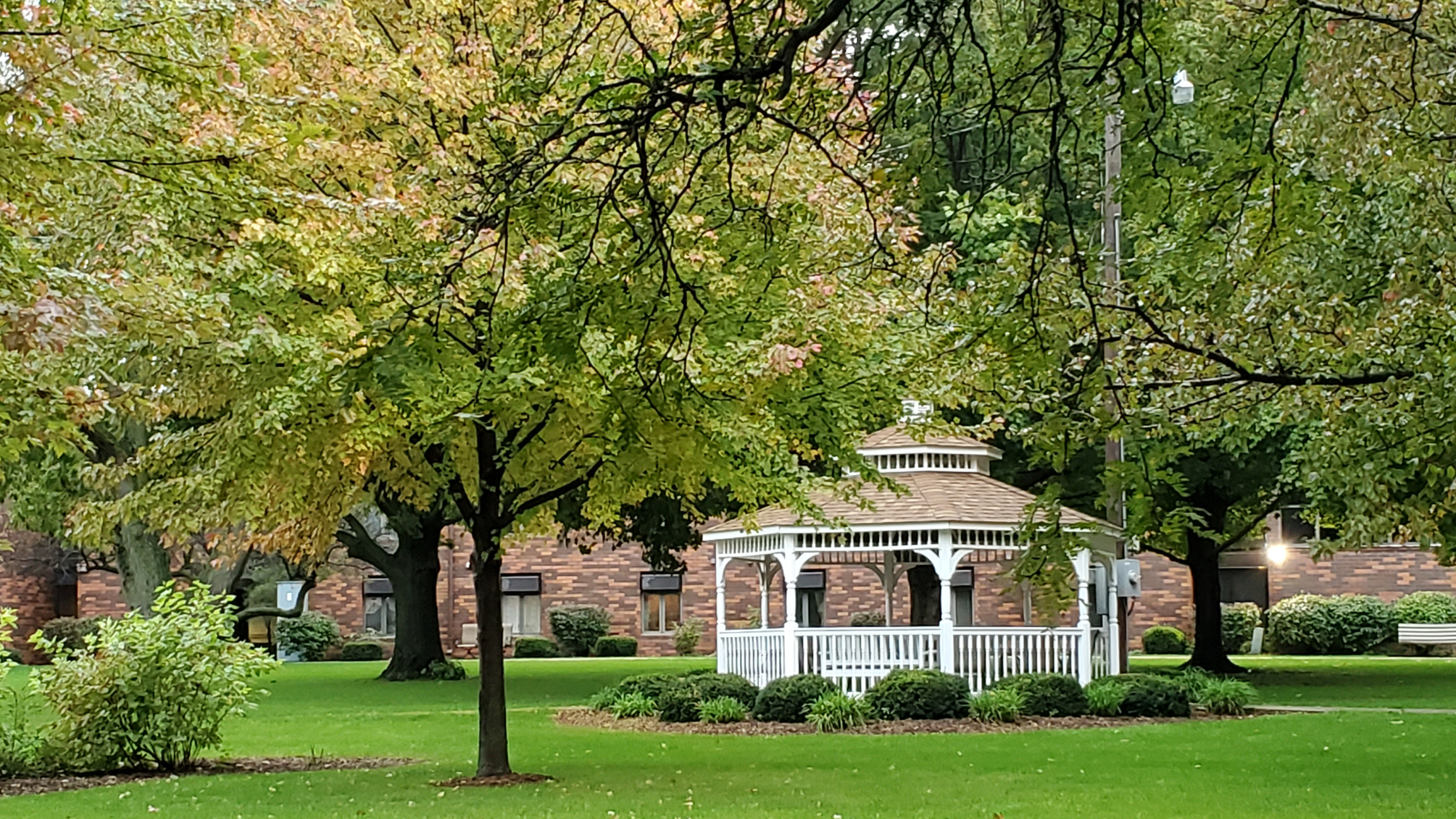 White gazebo located in green grass with trees
